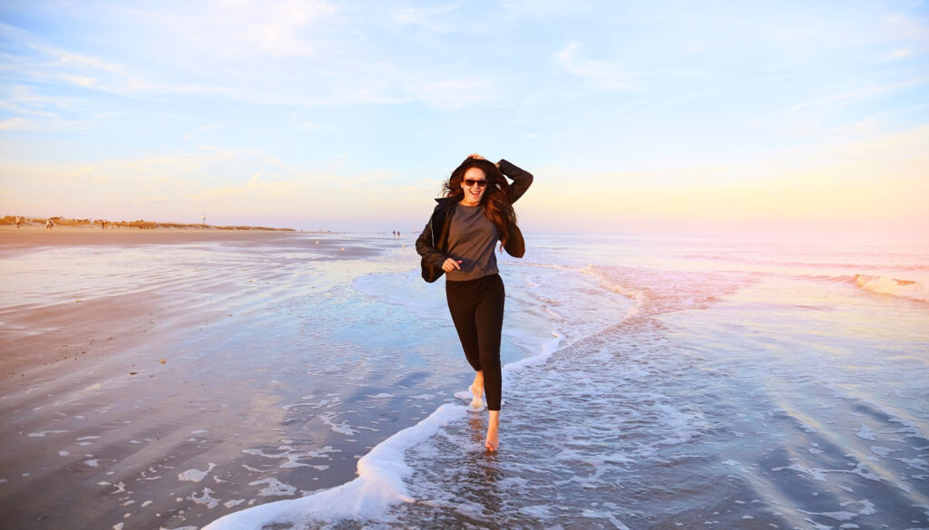 A photo of a clothed woman on a beach running toward the camera while the tide rolls in