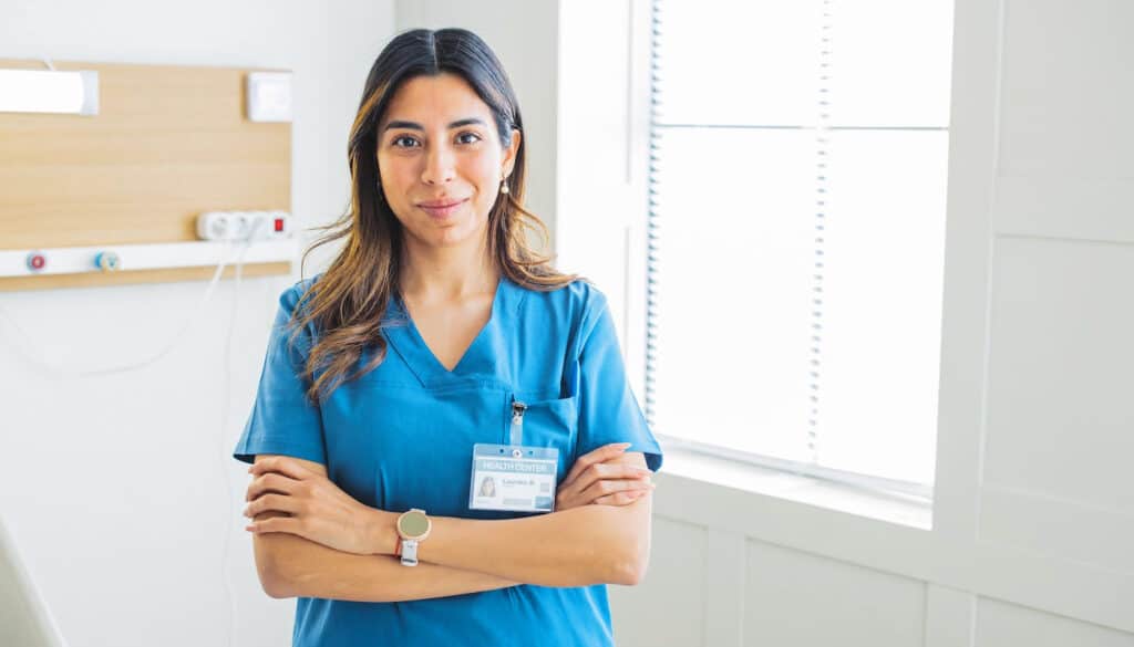 A nurse standing in a hospital room with her arms crossed.