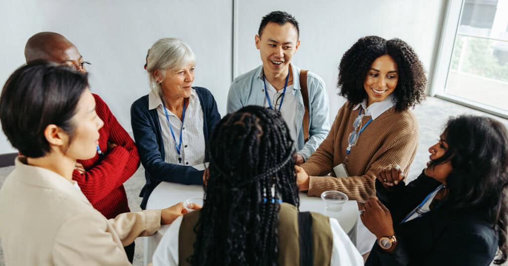 A group of people standing in a circle, engaged in conversation at an indoor event.
