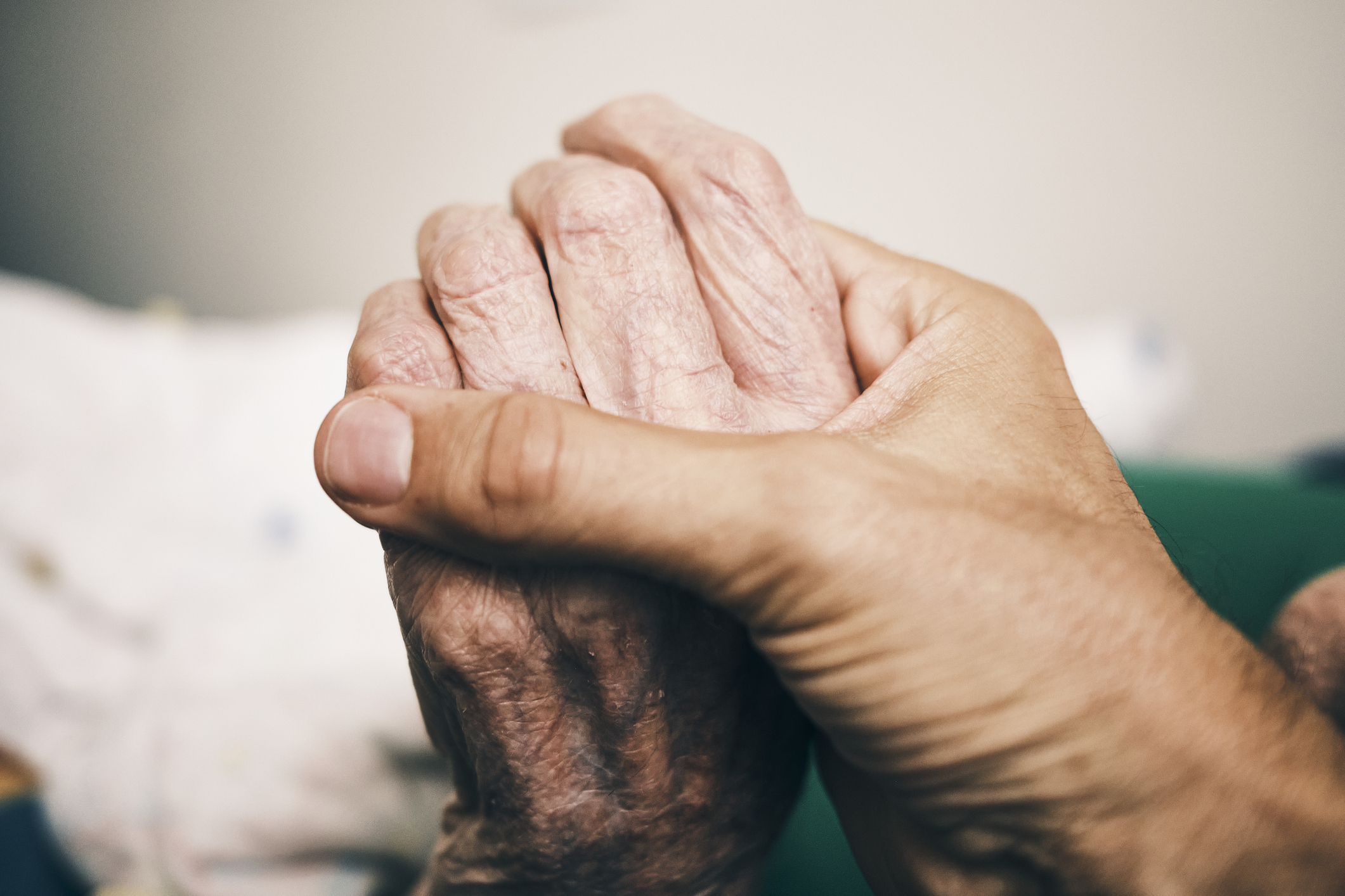 A younger person gently holding the hands of an older person, showing support and care.