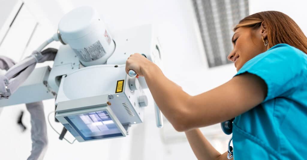 A healthcare worker in scrubs adjusts an X-ray machine in a medical facility.