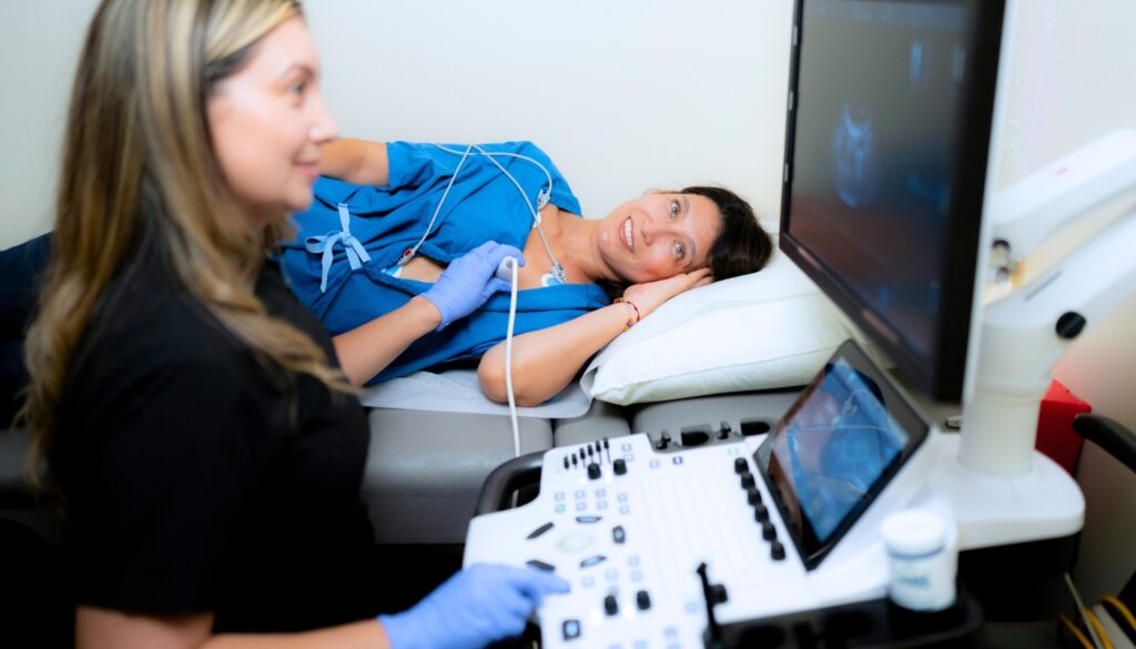 A healthcare professional performs an ultrasound scan on a woman lying on an examination bed, while monitoring the results on a screen.