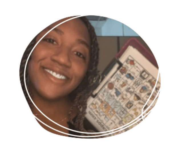 Smiling person with braided hair holding up a speech-generating device with various colorful symbols visible on the screen.