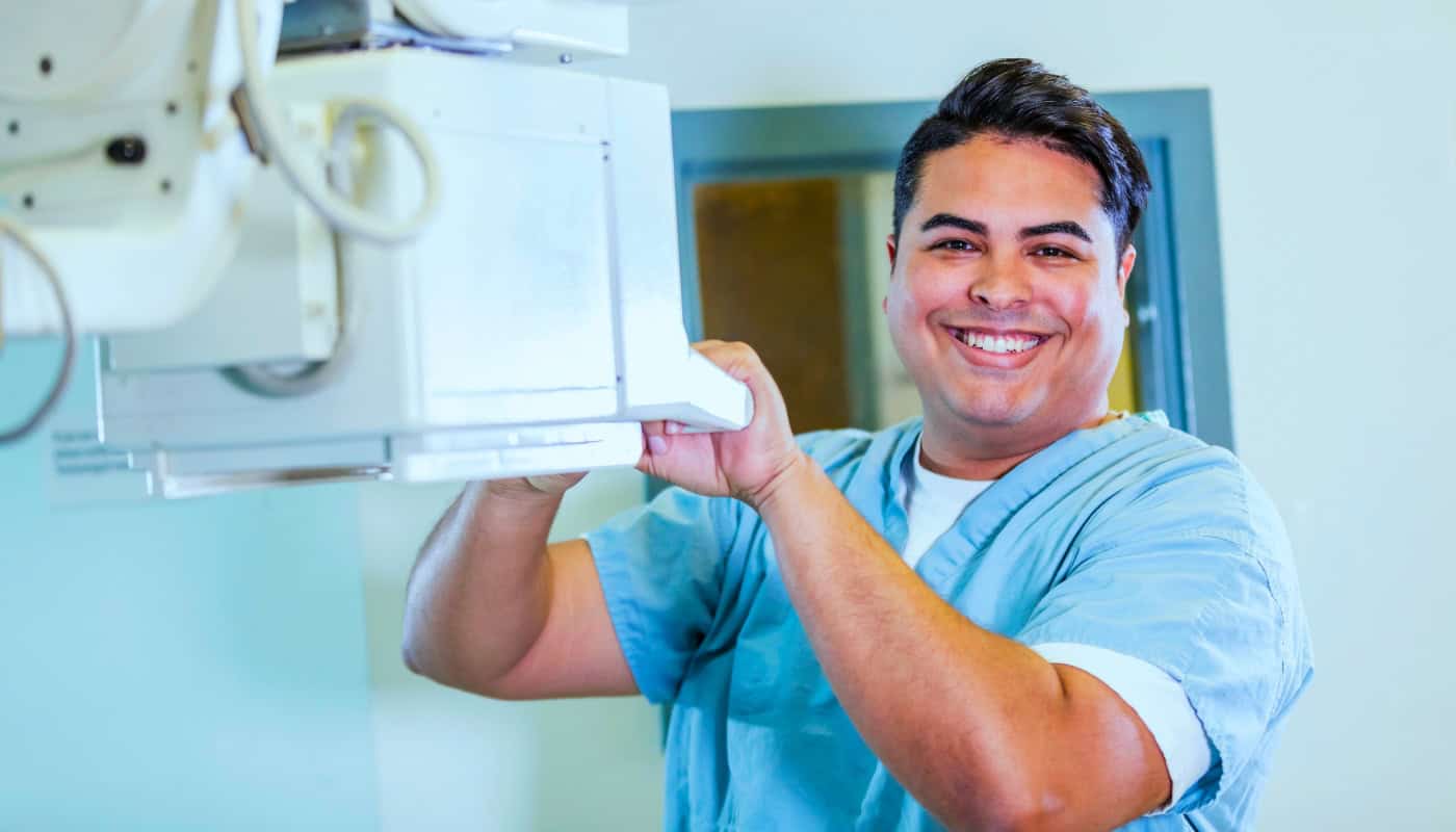 A smiling male radiologic technologist adjusting an X-ray machine.