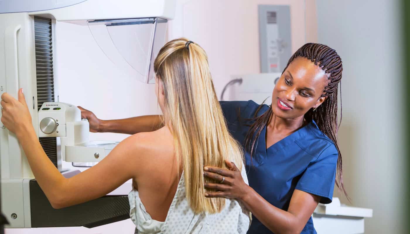 A technician positions a patient for a mammogram using a mammography machine.