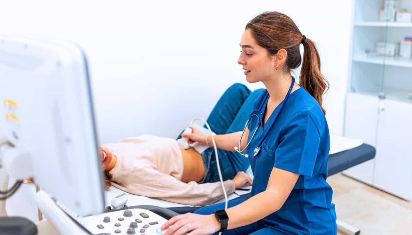 A medical professional in scrubs performing an ultrasound on a patient lying on an exam table.