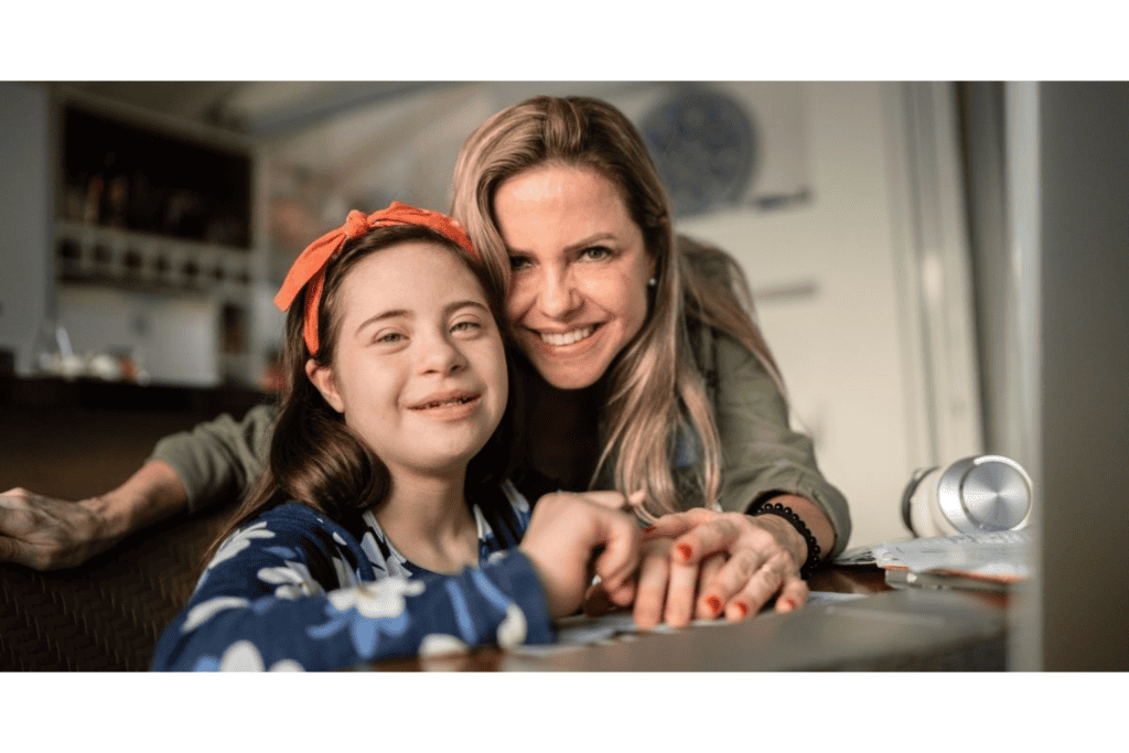 A woman and a girl with Down syndrome smiling together at a desk.