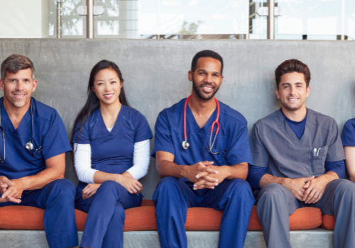 A photo of a group of young nurses sitting on a hospital bench smiling towards camera