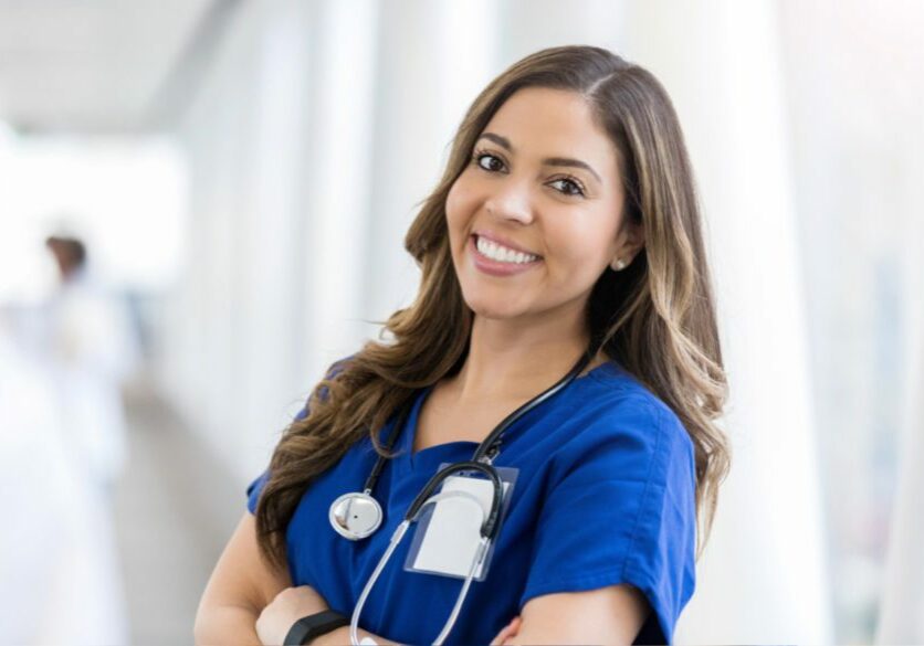 Image of a nurse smiling toward the camera while wearing scrubs and a stethoscope